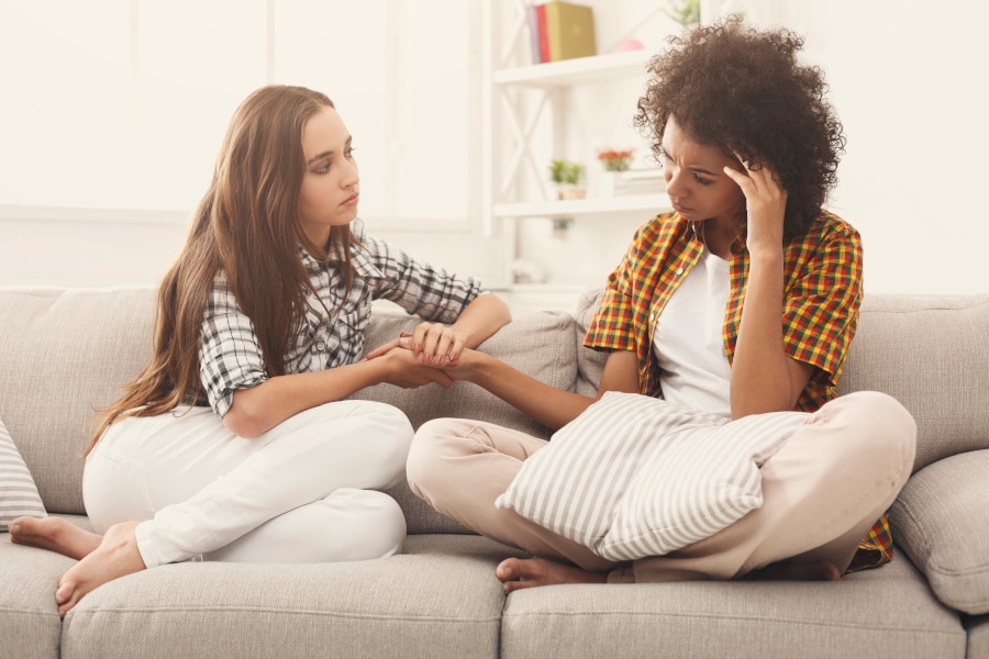 young woman being comforted by friend on couch