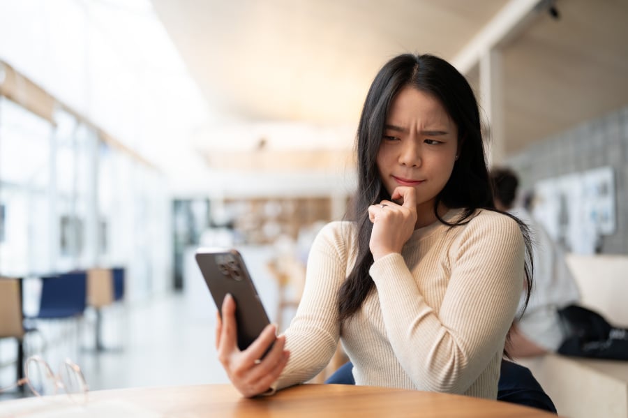 young asian woman looking at her phone with confused face