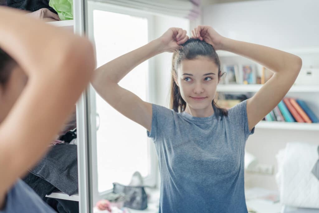 teen girl gently straightens her ponytail in mirror