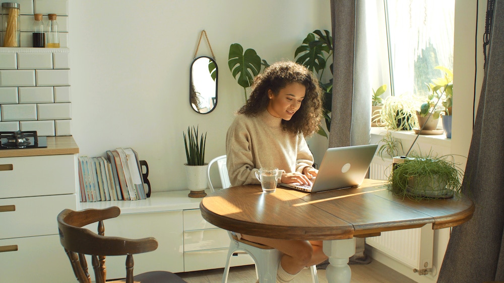 Young woman typing on laptop computer in a kitchen.